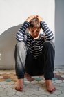 Unglückliches Kind, das auf dem Boden sitzt und den Kopf mit den Händen bedeckt, während es zu Hause unter häuslicher Gewalt leidet — Stockfoto