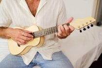 Обрезанный неузнаваемый мужчина на белой стене играет на укулеле — стоковое фото