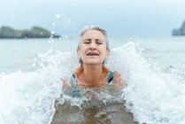 Активна старша сіра волохата жінка плаває в океанічній воді, насолоджуючись літом і практикуючи здоровий спосіб життя на морському узбережжі — стокове фото