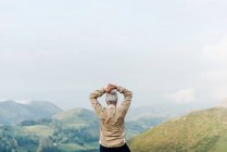 Visão traseira de viajante sênior irreconhecível levantando e esticando os braços de manhã em terreno montanhoso — Fotografia de Stock