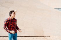 Habilidade jovem macho em camisa quadriculada realizando truque com bolas de malabarismo, enquanto em pé contra a estrutura de concreto contemporâneo na rua urbana — Fotografia de Stock