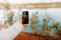 Recadrée personne méconnaissable tenant téléphone portable tout en regardant l'application de boussole au milieu d'une forêt avec lac — Photo de stock