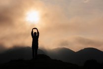 Силует анонімного дослідника руками над головою милуючись гірською місцевістю на тлі похмурого східного неба вранці в природі — стокове фото