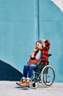 Independent handicapped mature female in wheelchair talking on mobile phone near painted wall on street — Stock Photo