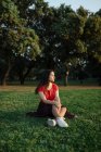 Транквільська жінка сидить на траві на лузі в парку і насолоджується заходом сонця влітку — стокове фото