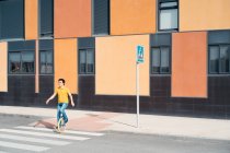 Uomo di talento in abbigliamento casual seduto su strada incrocio monociclo su zebra su strada urbana moderna con edificio colorato — Foto stock