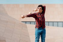 Skilled young male in checkered shirt performing trick with juggling balls while standing against contemporary concrete structure on urban street — Stock Photo