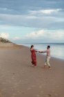 Fröhliches multiethnisches Paar hält Händchen und spaziert im Sommer am nassen Ufer entlang — Stockfoto