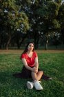 Спокойная женщина, сидящая на траве на лугу в парке и наслаждающаяся закатом летом — стоковое фото