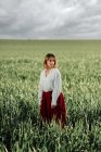 Ruhige junge Frau in altmodischer Bluse und Rock steht allein im hohen grünen Gras an bewölkten Sommertagen auf dem Land — Stockfoto