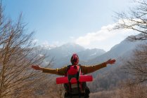 Обратный вид задумчивой путешественницы с рюкзаком, стоящим с вытянутыми руками в горах, смотрящей в сторону — стоковое фото