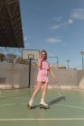 Повна довжина радісна жінка в рожевому вечірньому катанні на роликах фотографує миттєву фотокамеру на сонячному спортивному майданчику — стокове фото