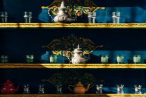 Calderas de cerámica y metal con vasos pequeños en estantes de colores en Marruecos - foto de stock