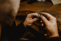 Анонимный ювелир держит незаконченное кольцо в грязных руках и проверяет качество в мастерской — стоковое фото