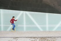 Full body side view of active young male in checkered shirt and jeans performing trick on unicycle near mirrored glass wall of contemporary building — Stock Photo