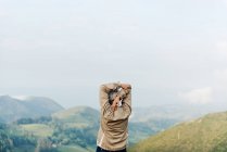 Обратный вид на неузнаваемую старшую женщину-путешественницу, поднимающую и вытягивающую руки утром на холмистой местности — стоковое фото