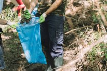 Група соціальних активних дітей з волонтером-чоловіком, який збирає сміття в мішок для сміття під час екологічної кампанії в літній природі — стокове фото