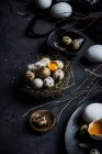 Из выше состава сырых куриных яиц на тарелках и перепелиных яиц в гнезде на черном фоне — стоковое фото