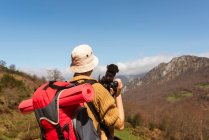 Visão traseira do mochileiro fêmea anônimo tirando fotos da paisagem montanhosa durante a viagem — Fotografia de Stock
