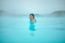 Seitenansicht eines jungen tätowierten Hipsters im Badeanzug, der im blauen Wasser zwischen Felsen posiert — Stockfoto