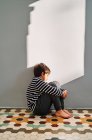 Seitenansicht eines unglücklichen Kindes, das auf dem Boden sitzt und den Kopf mit den Händen bedeckt, während es zu Hause unter häuslicher Gewalt leidet — Stockfoto