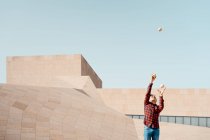 Опытный молодой мужчина в клетчатой рубашке, выполняя трюк с жонглированием мячами, стоя против современного бетонного сооружения на городской улице — стоковое фото