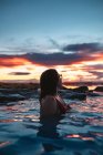 Vue latérale de la jeune femme en maillot de bain posant en eau bleue entre les rochers — Photo de stock