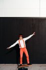 Corpo pieno di artista circo maschile in pantaloni rossi e cappello che esegue trucco sul bordo equilibrio contro parete nera — Foto stock