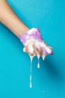 Рука врожаю анонімні жінки стискають губку ванни з білою піною на синьому фоні — стокове фото