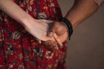 Crop anonymous woman in colorful dress and black man with bracelet on wrist holding hands while enjoying romantic moments together — Stock Photo