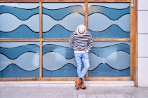 Дорослий латиноамериканець у модному одязі, спираючись на скляну стіну з абстрактним орнаментом і озираючись назад. — стокове фото