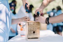 Високий кут врожаю невпізнавані батьки та дитина збирають дерев'яну коробку для гніздування птахів разом, беручи участь у екологічному проекті — стокове фото