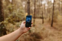 Cropped unrecognizable person holding mobile phone while looking at compass application in the middle of a forest — Stock Photo