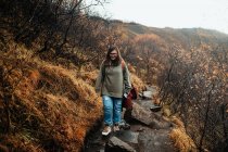 Jovem caminhante feminina em roupas de conforto com mochila andando no deserto contra o céu sombrio cinza — Fotografia de Stock