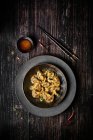 View from above of a plate of chili wontons on a wooden table next to chopsticks — Stock Photo