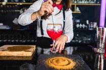 Обрізаний невпізнаваний жіночий банкір у стильному вбранні, що перемішує коктейль у склянці з довгою ложкою, що стоїть за стійкою в сучасному барі — стокове фото