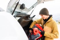 Vista laterale del contenuto avventuriero donna in piedi con zaino da viaggio vicino al bagagliaio dell'auto in montagna — Foto stock