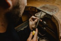 Bijoutier masculin anonyme utilisant un fichier pour façonner une bague en métal sur un établi en atelier — Photo de stock