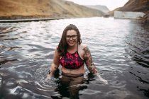 Giovane allegro hipster tatuato in costume da bagno in acqua tra le montagne — Foto stock