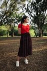 Trendy female in summer outfit standing on lawn in garden and looking away — Stock Photo