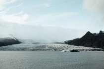 Pittoresca vista della superficie dell'acqua vicino incredibile ghiacciaio enorme tra colline rocciose e cielo blu — Foto stock