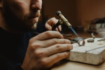 Goldschmied heizt mit einer Pusteblume winzige Metallornamente, während er Schmuck auf der Werkbank herstellt — Stockfoto