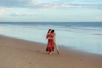 Liebender Mann umarmt Frau von hinten, während er den Sommertag zusammen am Strand verbringt — Stockfoto