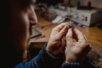 Анонимный ювелир держит незаконченное кольцо в грязных руках и проверяет качество в мастерской — стоковое фото