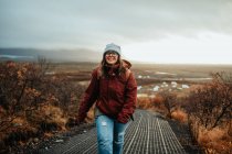 Giovane turista felice in inverno indossare andando su strada forestale e cielo nuvoloso — Foto stock