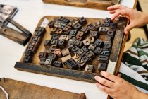 Кадрирование неузнаваемый мастер-мужчина работает с буквами из металла в деревянной рамке, стоя за столом в типографии — стоковое фото