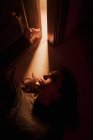 De cima de fêmea jovem silenciosa deitada no chão em quarto escuro com luz brilhando de porta aberta olhando para longe — Fotografia de Stock