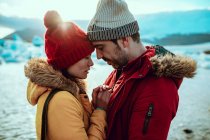Side view of young man and woman in winter wear standing on shore near water with ice — Stock Photo