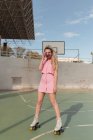 In voller Länge joyful fit weiblich in rosa Sundress Schlittschuhlaufen auf Rollen Aufnahmen auf Instant-Fotokamera auf sonnigem Sportplatz Blick auf Kamera — Stockfoto