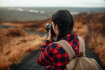 Back view of young tourist on walkway taking photo of valley from hill and cloudy sky — Stock Photo
